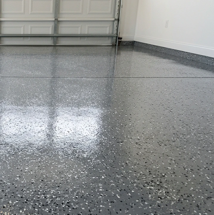 Close-up of a finished Rust-Oleum EpoxyShield style epoxy garage floor coating in glossy metallic grey with scattered decorative chips in grey, black and tan, showing the high-gloss reflective sheen characteristic of bonded epoxy
