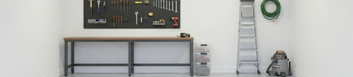 Close-up of a garage back wall showing the complete wall-storage approach — black metal pegboard mounted above a wood-top workbench with neatly arranged hand tools and a small power drill on white hooks, clear plastic storage bins stacked beside the workbench, a 6-foot aluminum step ladder leaning against the white-painted wall, a coiled green garden hose hanging on a wall hook above the ladder, a grey Ridgid shop vacuum on the floor in the right corner, pale grey epoxy floor