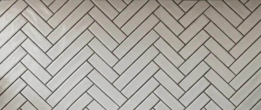 Close-up of classic white 3-by-6-inch ceramic subway tile backsplash laid in a herringbone zigzag pattern with thin charcoal grout lines, showing the Pinterest-favorite layout that elevates a basic subway tile install into a designed feature